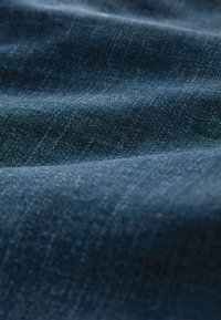 Temno modra denim tkanina z gladko teksturo, fino diagonalo tkanje ter subtilnimi odtenki in barvnimi variacijami.