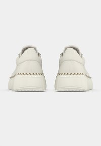 Fehér tornacipő sima felülettel, megemelt talppal és díszítő fonott részlettel a középtalpon. Minimalista kialakítás.