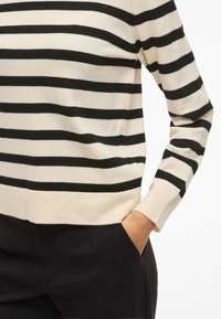 Striped sweater featuring horizontal black and cream stripes, knit fabric, ribbed cuffs, and side slits, paired with black trousers.