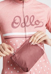 Pink cykeltrøje med lynlås, prydet med hvide polka dots og stripede detaljer. En lille bordeaux pouch bliver åbnet.