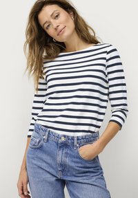 Witte en marineblauw gestreepte langemouwen top met een bootnek, gecombineerd met hoog getailleerde lichtblauwe jeans. Glad katoenmateriaal, casual pasvorm.