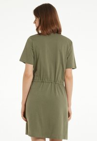 Olive zielona sukienka T-shirt z krótkimi rękawami, elastycznym w pasie, powyżej kolan, wykonana z miękkiego, lekkiego materiału o gładkiej teksturze.