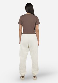 T-shirt croppato corto marrone a maniche corte con scollatura rotonda, abbinato a pantaloni della tuta bianchi larghi. Sneakers bianche con dettagli marroni.