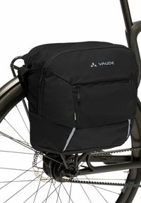 Schwarzer Rucksack aus strukturiertem Stoff, ausgestattet mit einer Frontreißverschlusstasche, reflektierenden Akzenten und einem schlanken Design, auf einem Fahrradträger montiert.