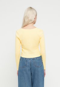 Żółta, długorękawowa bluzka o dopasowanym kroju i prążkowanej fakturze, zestawiona z wysokim stanem niebieskich dżinsów z tylnymi kieszeniami.