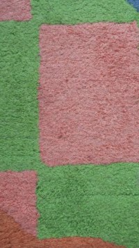 Kleurig tapijt met textuur, bestaande uit pluche groene, roze en oranje secties in geometrische vormen, met een zachte, harige oppervlakte.