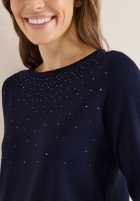 Marineblauer Pullover mit Rundhalsausschnitt, der ein strukturiertes Design mit verstreuten kleinen Metallnieten auf der oberen Vorderseite aufweist. Glattes Gewebe.
