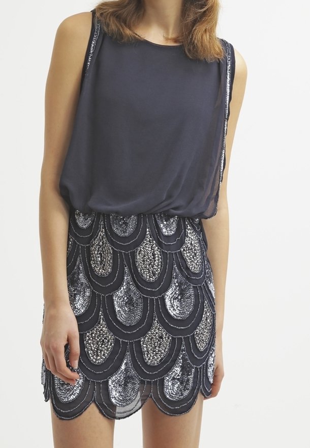 Haut sans manches bleu marine avec une silhouette fluide, associ é à une jupe courte avec un design en sequins ondulés argentés et bleu marine foncé.