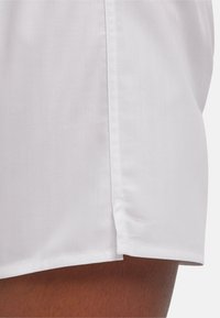 Shorts blancs présentant une subtile texture en chevron, avec une fente latérale et des coutures nettes le long de l'ourlet et de la couture.