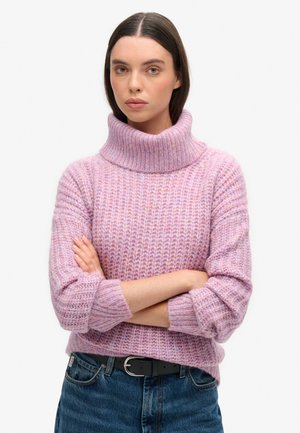 Lilla strikket sweater med høj, foldet krave. Har strukturerede lodrette linjer og brede ærmer, parret med mørk denim jeans.