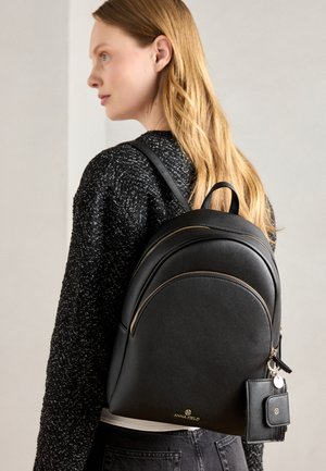 Black leather backpack with gold hardware, rounded shape, and a front zip pocket. Accompanied by a small matching cardholder attached.