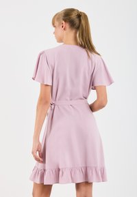 Ljust rosa klänning med fjärilsärmar, åtstramad midja och volangkant. Tillverkad av mjukt tyg, med en enkel baksidedesign och en minimalistisk look.