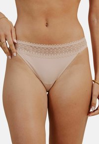 String nu avec un bord en dentelle à la taille, tissu doux et design minimaliste. Doté de bords délicats en feston le long de la ceinture.