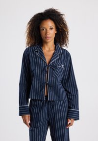Ensemble de pyjama à rayures bleu marine comprenant un haut court noué à l'avant avec des accents blancs, et un pantalon assorti avec une taille élastique et des poches.