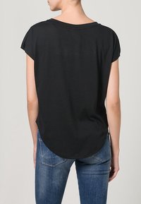 Zwarte korte mouwen t-shirt met een ontspannen pasvorm, gebogen zoom en zachte textuur, gecombineerd met blauwe denim jeans met een lichte vervaging.