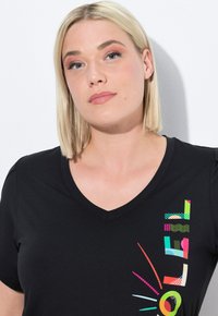 Zwarte V-hals t-shirt met meerkleurige geometrische en grafische patronen aan de linkerkant. Korte mouwen, zachte textuur.