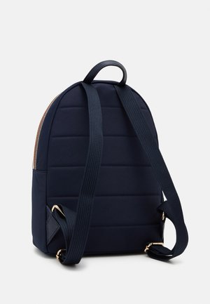 Petit sac à dos bleu marine avec dos rembourré, bretelles en tissu réglables, poignée supérieure et fermeture éclair dorée visible de dos.