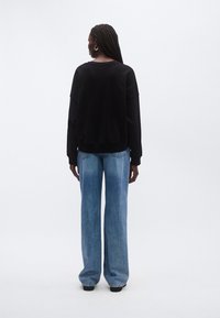 Υπερμεγέθη μαύρο φούτερ με μακριά μανίκια και ριμπ μανσέτες σε συνδυασμό με χαλαρά εφαρμοστά ανοιχτό μπλε τζιν, και τα δύο σε casual στυλ.