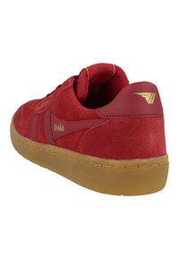 Baskets en suede rouge avec une finition texturée, col rembourré et semelle en gomme. Détail du logo doré sur le côté et accent sur le talon.