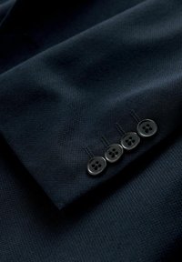 Marineblauer Stoff mit strukturierter Webart, versehen mit vier schwarzen Knöpfen an einer Manschette. Die Knöpfe haben vier Löcher und sind gleichmäßig angeordnet.