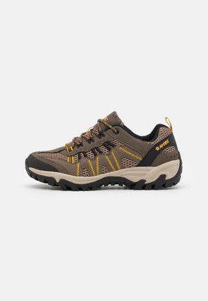 Scarpa da trekking marrone con tomaia in mesh e materiale sintetico, accenti gialli, suola in gomma e puntale rinforzato. Presenta un colletto imbottito e chiusura con lacci.