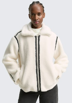 Witte fleecjacket met een ritsluiting, zwarte accentstrepen langs de mouwen en een spread collar. Zachte textuur en oversized pasvorm.