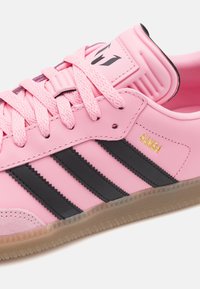 Ljusrosa sneakers med svarta tre ränder, slätt syntetiskt material, texturerad gummisula och guld "Samba" logodetalj.