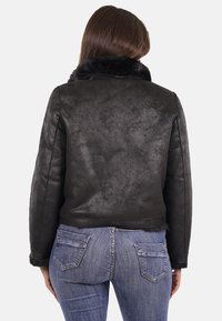Giacca in faux pelle nera con colletto di pelliccia. Presenta una texture liscia e un design aderente. Indossata con jeans blu, mostra la vista posteriore.