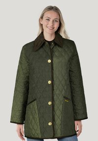 Olivgrüne gesteppte Jacke mit einem Cordkragen, goldenen Knöpfen und Seitentaschen. Auffälliges Rautenmuster und kontrastierender Besatz.