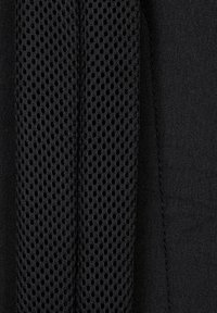 Närbild av svart tyg med en vertikal remsa av andningsbart mesh med cirkulära hål bredvid ett solidt vävt material.