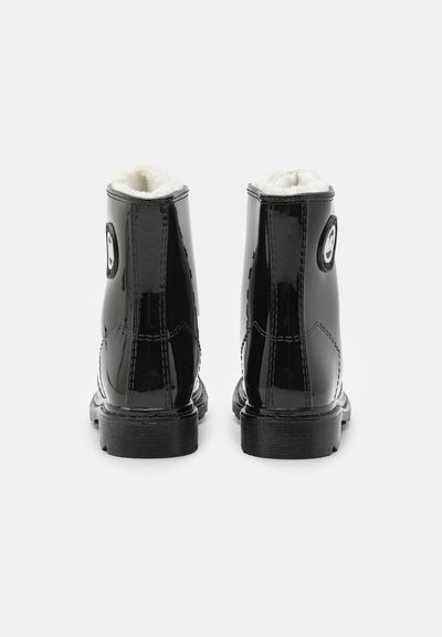 Bottes chelsea en cuir verni noir avec doublure en fausse fourrure blanche, patch logo rond sur le côté et semelle en caoutchouc texturée. Fini lisse et brillant.