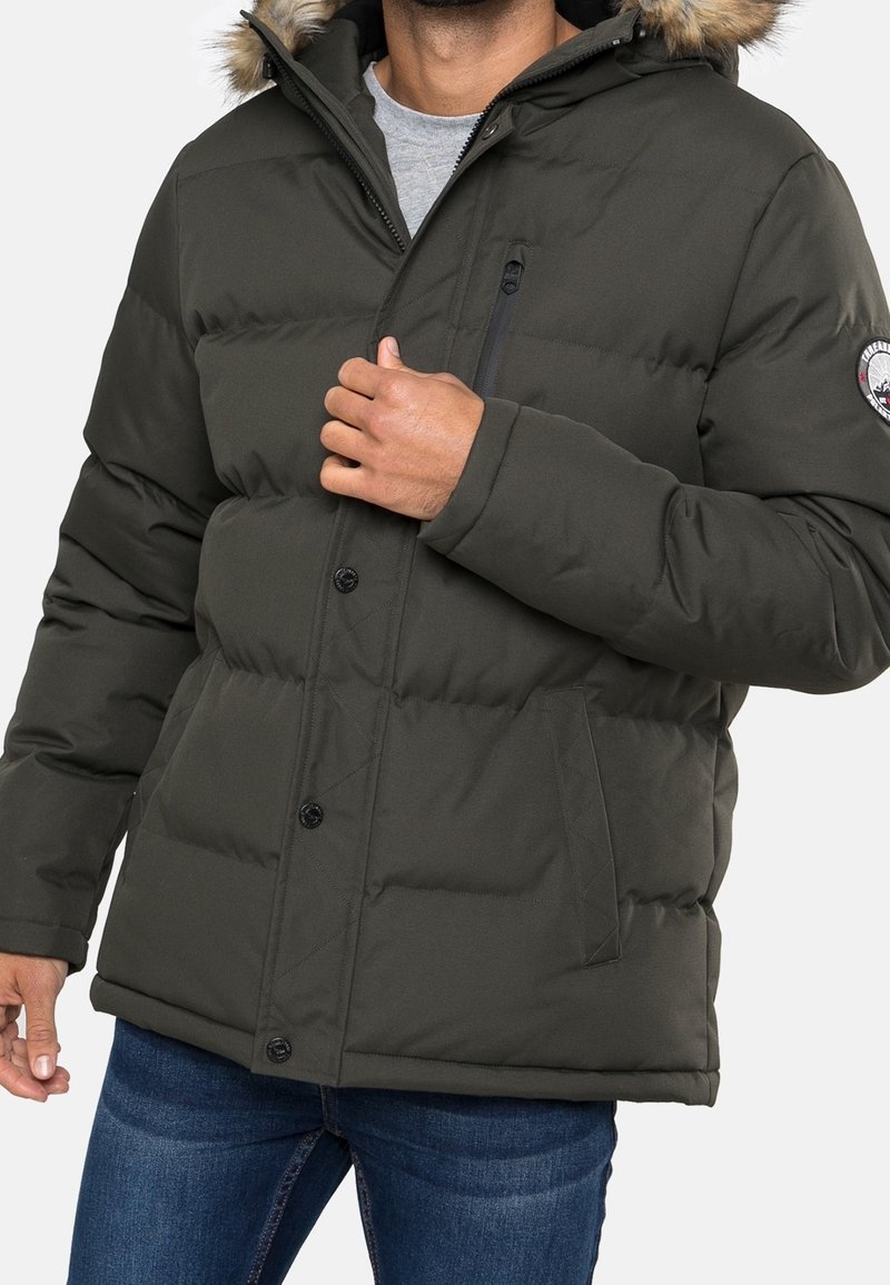 Zimní bunda tmavě zelené barvy s výplní, s kapucí lemovanou kožešinou, na zip kapsa na hrudi a černé patentky. Má prošívaný design.