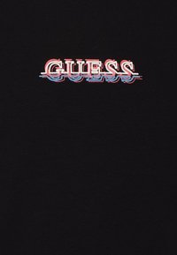 Camiseta de algodón negra con la palabra "GUESS" en letras 3D en negrita de color rojo y azul, con un efecto de desenfoque que crea profundidad y dimensión.