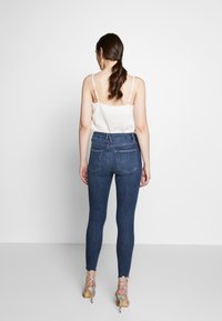 Mörkblå skinny jeans med hög midja, med bakfickor, lätt fransning vid fållen, i kombination med en ljus linne och klackar.