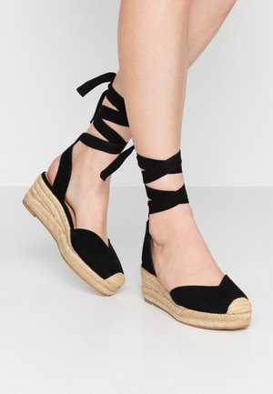 Czarne zamszowe espadryle z plecioną jucie, z okrągłym noskiem i wiązaniami na kostce dla pewnego dopasowania. Gładka cholewka i teksturowana podeszwa.