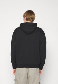 Sudadera negra con capucha, de fit relajado, con puños y dobladillo de canalé, y tejido suave. La parte trasera no presenta estampados ni adornos.
