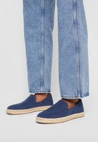 Espadrillas blu navy con tomaia in tessuto, suola in juta e design a intaglio; abbinate a jeans in denim azzurro chiaro con vestibilità dritta.