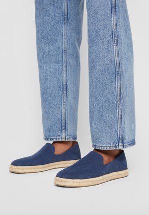 Espadrilles de color azul marino con parte superior de lona, suela de yute y diseño recortado; combinadas con jeans de mezclilla azul claro de corte recto.