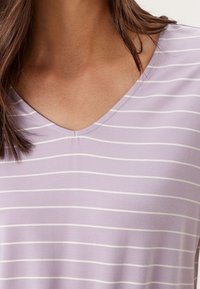Top de pico lila con rayas horizontales blancas, textura suave y detalle de costura central. Ideal para looks casuales.