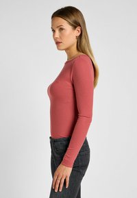 Ribbad långärmad topp i dammros, figurnära design med rund urringning. Kombineras med svarta högmidjade jeans med standardpassform.