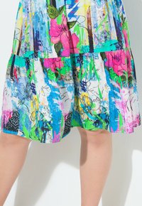 Vestido colorido con una mezcla de flores vibrantes y patrones abstractos. Fabricado en un tejido ligero con un diseño en capas, principalmente en azul y rosa.