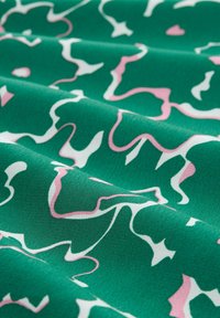 Tela verde con un patrón ondulado en blanco y rosa, textura suave, pliegues que crean profundidad, acabado liso y un contraste de colores vibrante.