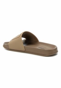 Sandalias de slide beige con parte superior de goma, plantilla contorneada y suela texturizada. Presentan una correa ancha a través del empeine y un branding sutil.