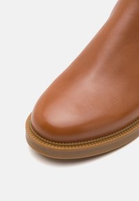 Bruine leren laars met een ronde neus, gladde textuur en een contrasterende rubberen zool met een gestikte detail langs de rand.