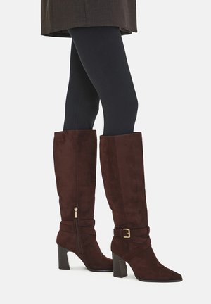Hnědé semišové kozačky po kolena s špičatou špičkou, s přezkou na kotníku a texturovaným povrchem. Mají robustní podpatek a postranní zip.