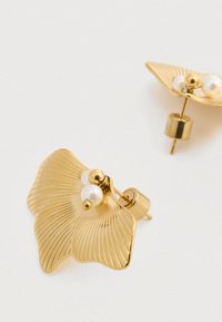 Χρυσές σκουλαρίκια σε σχήμα φύλλων γκίνκγκο, με υφή και δύο μικρές λευκές πέρλες στο κέντρο. Κλείσιμο με πίσω κούμπωμα.