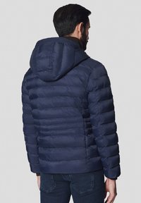 Granatowa kurtka puchowa z kapturem, z pikowanym wzorem i ściągaczem na dole. Miękka, teksturowana tkanina o luźnym kroju.