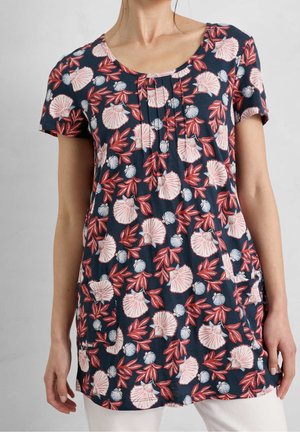 Woman wearing navy blue short-sleeve tunic with pink and red shell and leaf pattern, front pockets, and pleats at neckline.