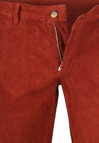 Roestkleurige corduroy broek met gedeeltelijk opengetrokken zilveren rits en bruine knoopsluiting bij de tailleband, waarbij de stoftextuur en stiksels zichtbaar zijn.