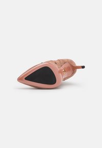 Escarpin beige en daim à bout pointu avec une semelle rose brillante, présentant une texture lisse et un insert en caoutchouc noir contrastant.